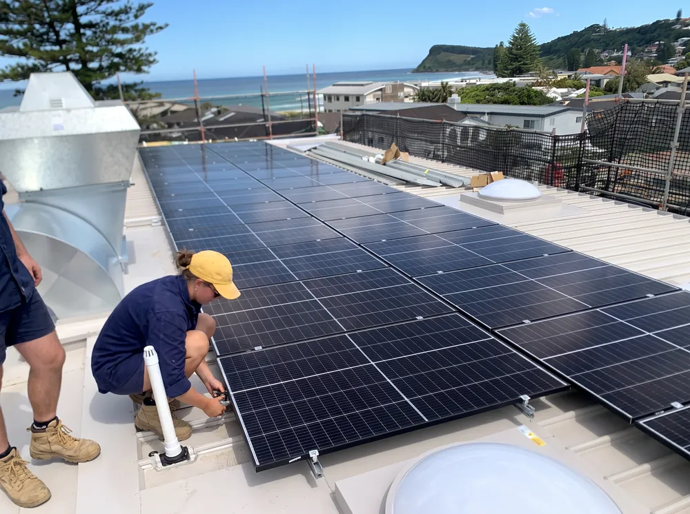 A Solar Start installer fitting an all-black array above the Northern NSW coastline